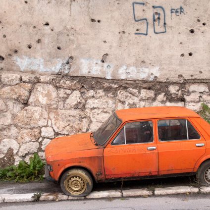 Travel photography, an old orange Yugoslavian car (Zastava) in front of a building with bullet holes